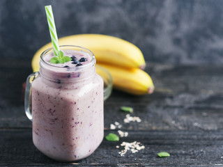 A jar of dark smoothie with blueberries and banana on a wooden table