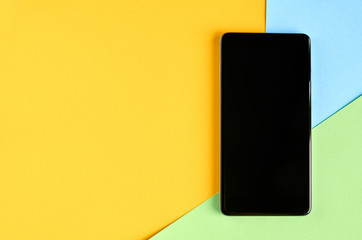 Black cellphone on yellow and blue background composition, mobile phone.