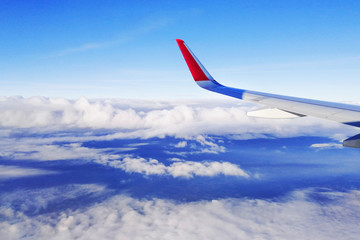 view from the airplane porthole to the wing and bright blue sky with white clouds horizontal orientation