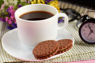 Coffee cup with cookies, alarm clock, flowers, mascara, on pink background composition.