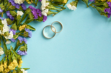 Golden rings with colored flowers on blue background composition, wedding template.