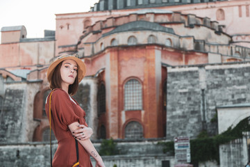 Fototapeta na wymiar Beautiful girl with orange colored dress posing with Hagia Sophia during sunset from Istanbul