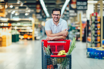 Handsome man shopping in supermarket pushing trolley and smilling.