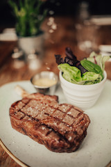 A close up shot of a beef fillet steak with sea salt served on a ceramic plate with salad and sauce. Concept of restaurant, food and culinary.