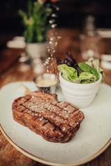 A close up shot of a beef fillet steak with sea salt served on a ceramic plate with salad and sauce. Concept of restaurant, food and culinary.