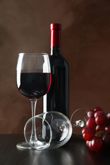 Grapes, bottle and glass with wine against brown background, copy space