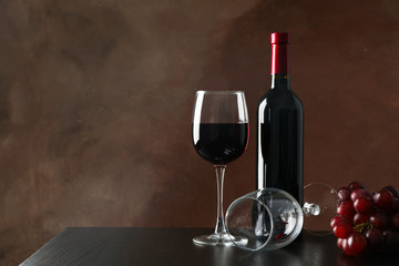 Grapes, bottle and glass with wine against brown background, copy space