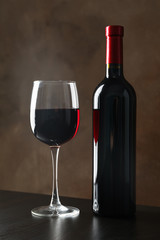 Bottle and glass with wine against brown background, copy space