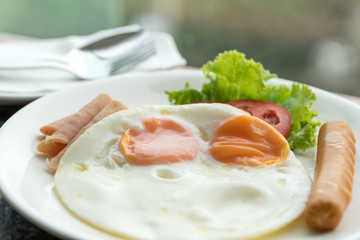 Breakfast, fried egg, ham, sausage on white dish.