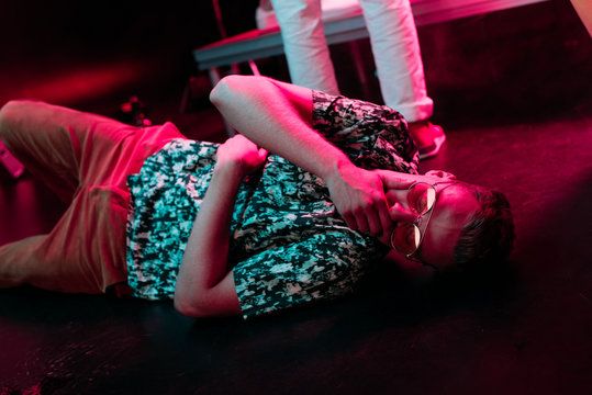 sick man lying on floor in nightclub and covering mouth with hand