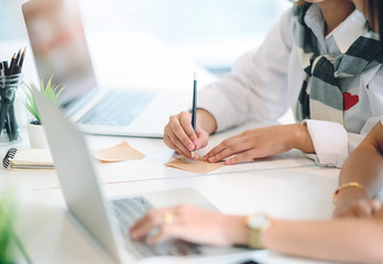 woman writing on notepad with pencil while working in office.