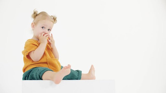Cute blonde baby girl eats apple against white background
