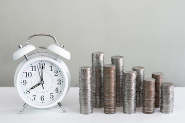 Alarm clock and coin piles arrange into growth chart on white background, finance and business concept