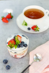 Oatmeal with yogurt with strawberries and blueberries with spoon and cup of tea