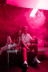 Fototapeta na wymiar smiling man with beer sitting near girl in nightclub during rave