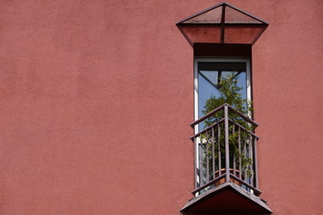 small triangular balcony in the house with a coral facade and potted flowers on fence. a place to...