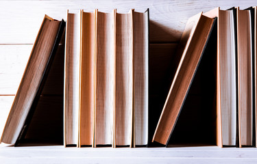 Old books with yellow pages stand on a white wooden shelf