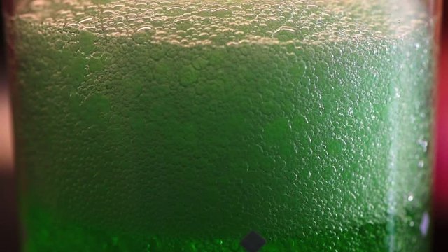 Zooming view of green estragon drink pouring into water glass with lot of bubbles and foam. Full HD 60fps footage with shallow depth and blurring bokeh.