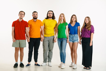 Young man and woman weared in LGBT flag colors on white background. Caucasian models in bright shirts. Look happy together, smiling and hugging. LGBT pride, human rights and choice concept.