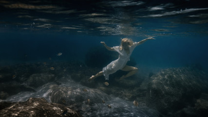 Obraz premium Woman in white swims underwater in the sea