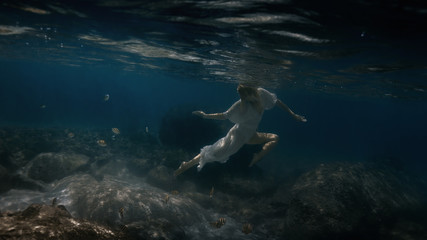 Woman in white swims underwater in the sea