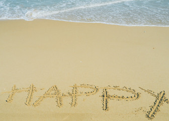 Happy wording written on sand next the sea. relaxing and enjoying summer vacation at the beach.