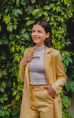 Beautiful young girl among the greens in stylish and classic yellow suit. Portrait. Fashion.