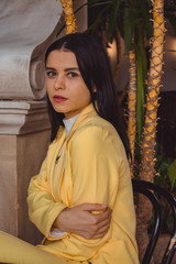 Beautiful young girl among the greens in stylish and classic yellow suit. Portrait. Fashion.