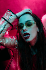 attractive girl in sunglasses with lsd on tongue in nightclub with pink smoke