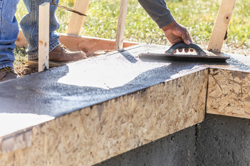 Construction Worker Using Wood Trowel On Wet Cement Forming Coping Around New Pool