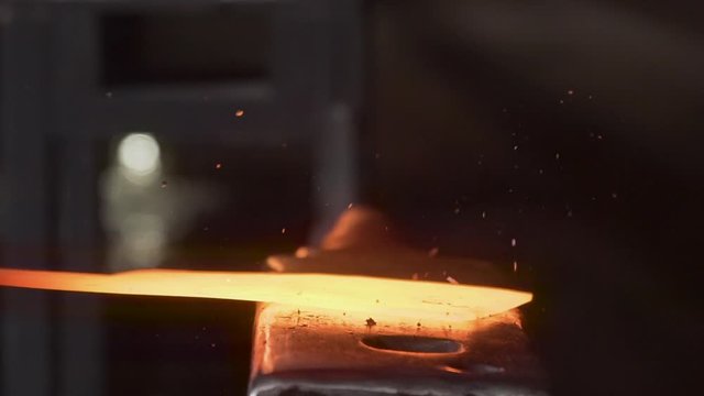 Close-up of a hot yellow glowing knife being forged on an old anvil outside in the darkness of the night - Slow Motion
