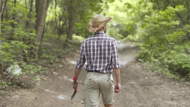 Outdoors man holding axe walks down woodland road