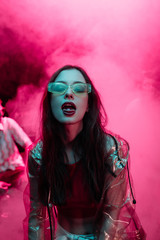 beautiful girl in sunglasses with lsd on tongue in nightclub with pink smoke