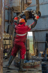 Work driller in red uniform, in helmet and goggles. He with the help of an elevator hangs drill...