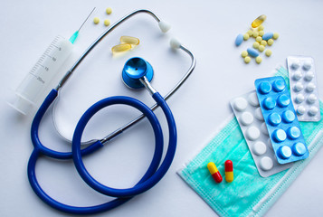 Top view of flat lay: medical supplies doctor, funds for the treatment of the patient - the stethoscope, protective mask, pills, thermometer, syringe on the background of a white textured rough sheet