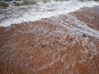 Frothy waves of the sea on the sandy beach. Foamy wave rolls