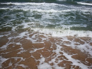 Frothy waves of the sea on the sandy beach. Foamy wave rolls
