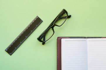 Conceptual layout on a green background. A detailed notebook, glasses and a ruler. Flat lay.