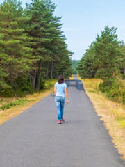 Fototapeta premium Rear view of a woman in jeans walking on road in a forest