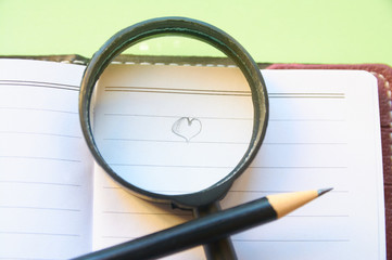 A heart drawn in a notebook with a pencil under a magnifying glass.