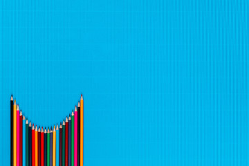 A bunch of crayons arranged like a parabola on a blue background , shot from above, aligned at the bottom left.