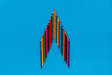 A bunch of crayons forming an arrow head on a blue background, shot from above, arranged in the center.