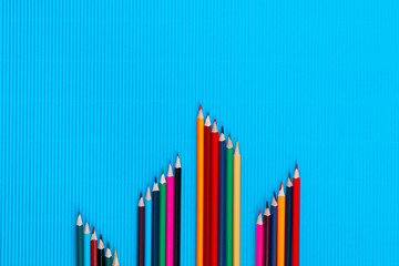 A bunch of crayons in small columns on a blue background, shot from above , arranged at the bottom, closeup.