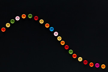 A wave made from buttons on a black background , shot from above, closeup.