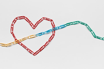 An arrow made from paperclips pointing upwards passing through a heart on a white background, shot from above, closeup.