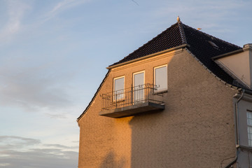 Hausfassade mit Balkon und Krüppelwalmdach im Abendlicht
