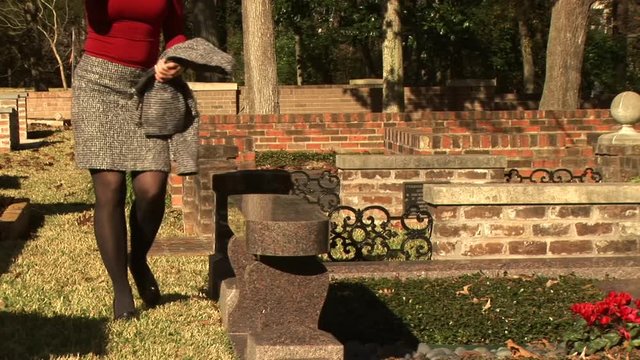 woman walks to a grave, kneels and prays