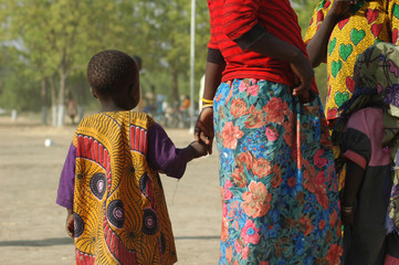 Cameroon, Maga. Young child holding the hand of a woman, and looking towards the horizon, both wearing colourful outfits made of local fabrics with colourful patterns 
