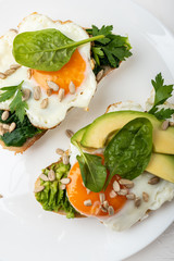 Breakfast on the white background. Fried eggs on a toasts bread with avocado, spinach and seeds on a white plate with cup of tea. Top view.