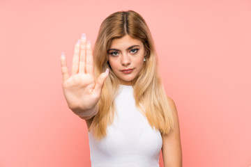 Teenager girl over isolated pink background making stop gesture with her hand